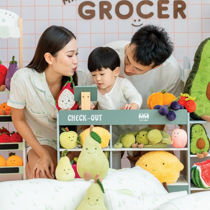 A family of three — mother, father, and baby boy — smiling together while wearing matching outfits from Le Petit Society's sleepwear collection, featuring a print of pastel green pears. 
