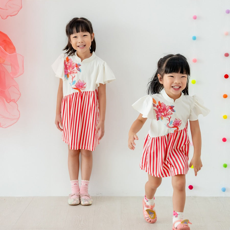 ChatGPT said:

Two young girls wear matching cream-and-red striped dresses from the Le Petit Society x Sheila Sim CNY 2026 lotus collection. The dresses feature a cream bodice with vibrant lotus motifs and flutter sleeves, paired with a bright red verti