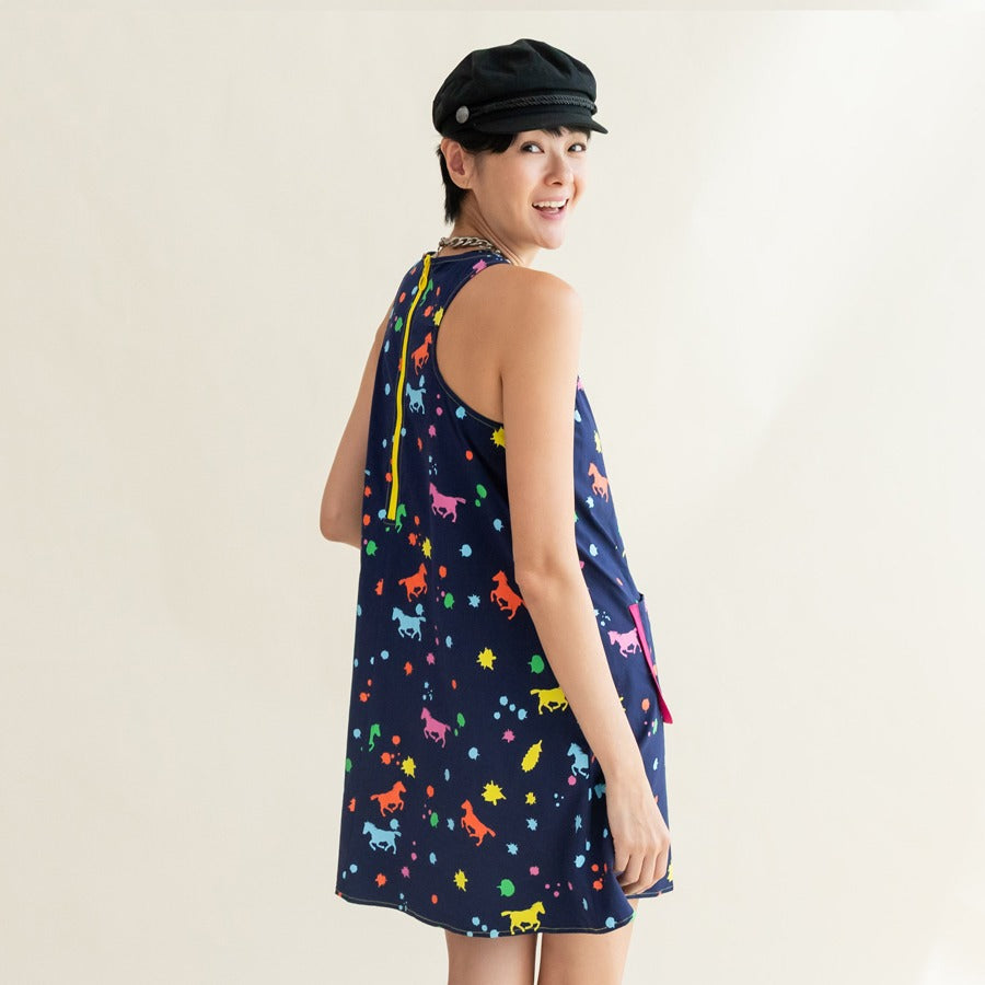 A woman looking over her shoulder and smiling, showing the back-tie detail of the navy rainbow horse-print dress from the Le Petit Society x Sheila Sim CNY 2026 Rainbow Horse Collection.