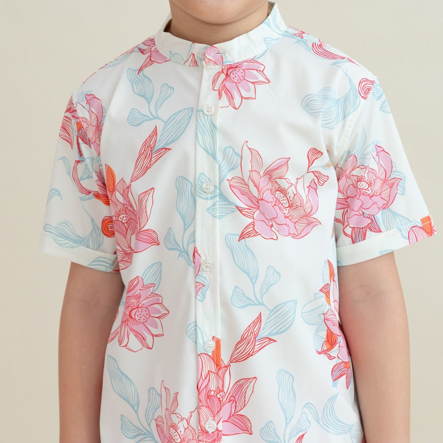 A close-up view of the boys’ mandarin-collar shirt from the Le Petit Society x Sheila Sim CNY 2026 Lotus Collection. The fabric showcases intricate lotus blooms in coral and blush, layered with sky-blue leaves and flowing linework. The neat button placket