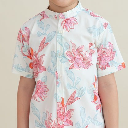 A close-up view of the boys’ mandarin-collar shirt from the Le Petit Society x Sheila Sim CNY 2026 Lotus Collection. The fabric showcases intricate lotus blooms in coral and blush, layered with sky-blue leaves and flowing linework. The neat button placket