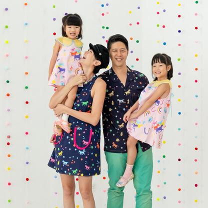A family of four dresses in the Rainbow Horse pieces from the Le Petit Society x Sheila Sim CNY 2026 Collection. The father wears the navy men’s shirt, the mother the matching navy dress, while the daughters wear pastel pink Rainbow Horse dresses. Bright 