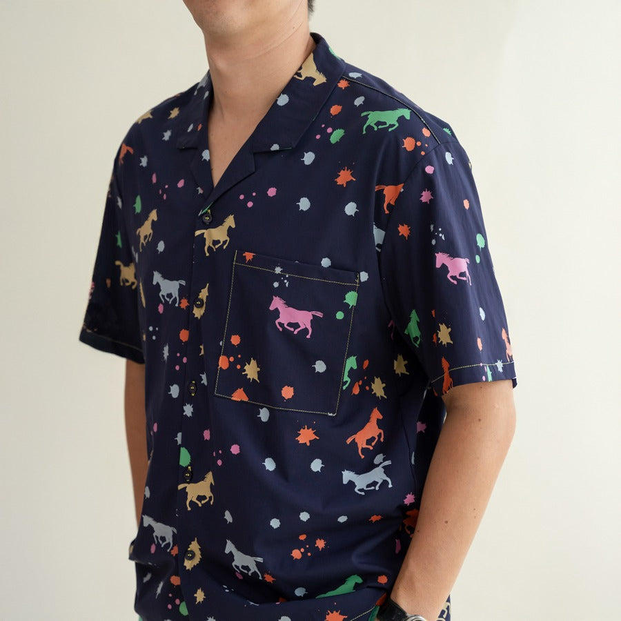 A close-up of the men’s Rainbow Horse shirt from the Le Petit Society x Sheila Sim CNY 2026 Collection. The navy fabric features colourful horses, splashes and tiny star-like dots, with a neatly stitched front pocket showcasing a pink horse motif. The det