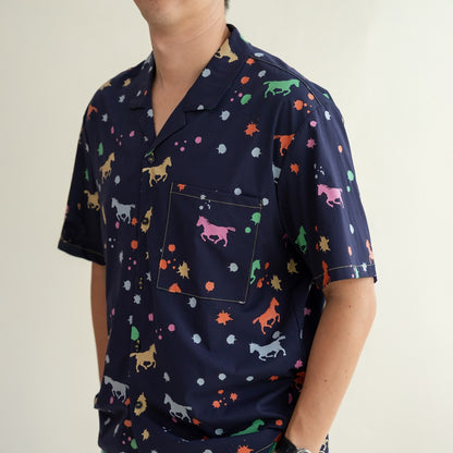 A close-up of the men’s Rainbow Horse shirt from the Le Petit Society x Sheila Sim CNY 2026 Collection. The navy fabric features colourful horses, splashes and tiny star-like dots, with a neatly stitched front pocket showcasing a pink horse motif. The det