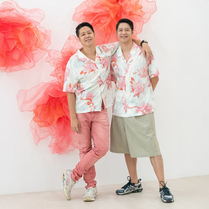 Two men stand side by side wearing matching shirts from the Le Petit Society x Sheila Sim CNY 2026 Lotus Collection. The light, floral print in coral and sky blue adds a soft festive touch, while their relaxed poses and easy smiles create a friendly, cele