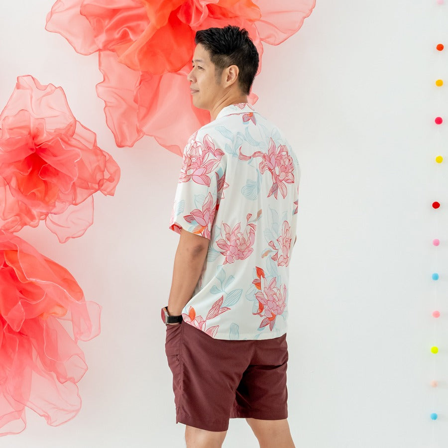 A man stands in profile wearing the men’s shirt from the Le Petit Society x Sheila Sim CNY 2026 Lotus Collection. The coral and sky-blue lotus motifs wrap softly around the back of the shirt, creating a light and airy look against the white base. He pairs