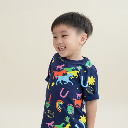 A close-up of a young boy laughing while wearing the Rainbow Horse tee. The colourful horses, rainbows and stars stand out vividly against the deep navy fabric, capturing the bright and cheerful mood of the design.