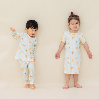 A little boy and girl wearing matching sleepwear from Le Petit Society, featuring pastel green stripes and a print of breakfast food.
