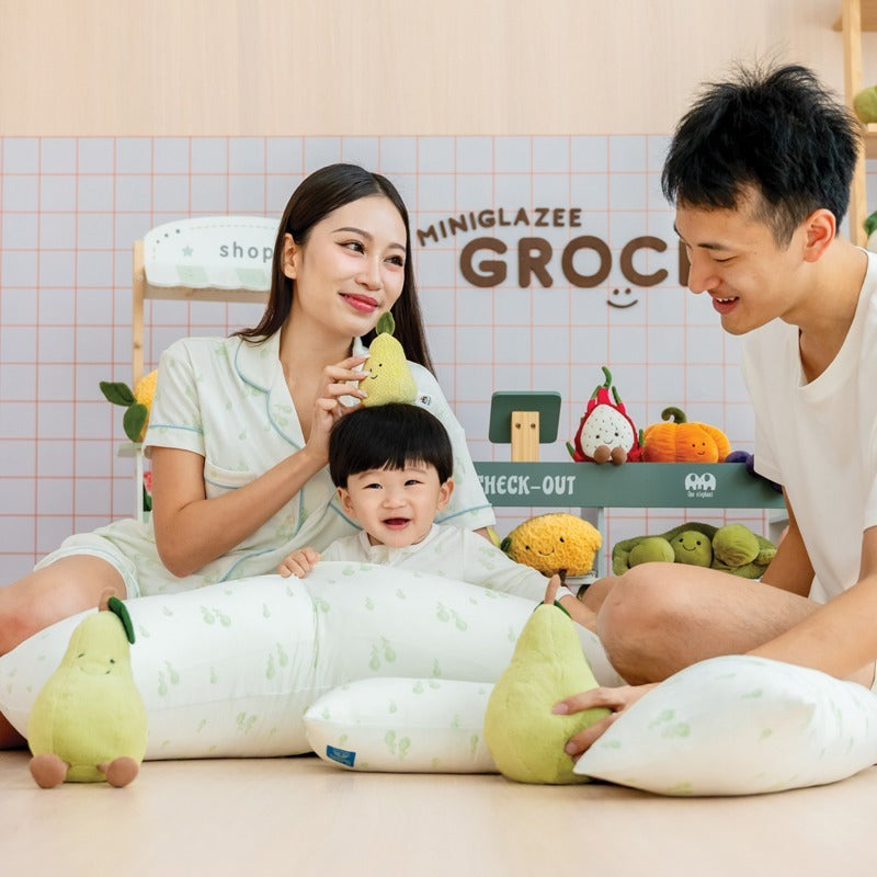 A family of three — mother, father, and baby boy — smiling together while wearing matching outfits from Le Petit Society's sleepwear collection, featuring a print of green pears.