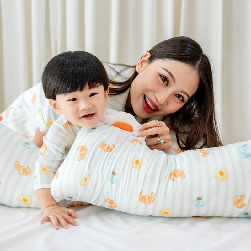 A mother and her baby boy wearing matching sleepwear and holding a pillow, all adorned with a playful breakfast food print from Le Petit Society.