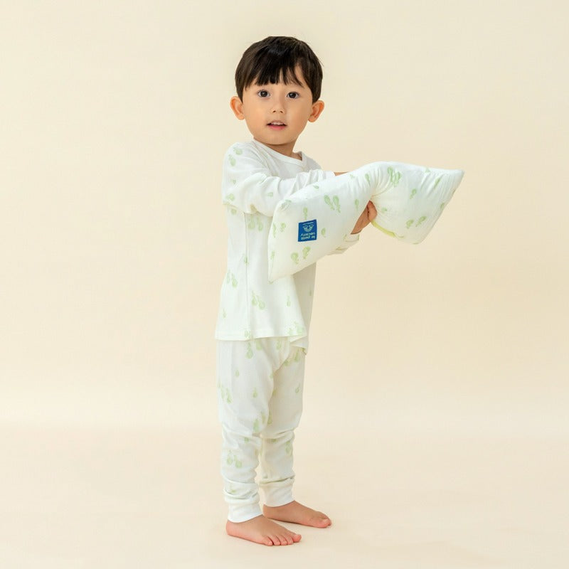A little boy wearing a pyjamas set from Le Petit Society, with a pillow in a matching print of green pears.
