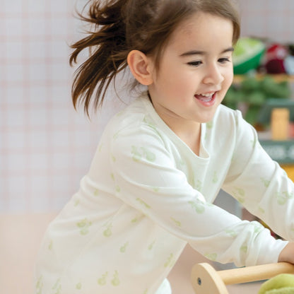 A little girl wearing a pyjamas set from Le Petit Society, featuring a soft bamboo fabric and a print of green pears.