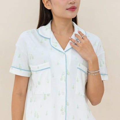 A closeup image of an adult woman wearing a pyjamas set from Le Petit Society, featuring a print of green pears.