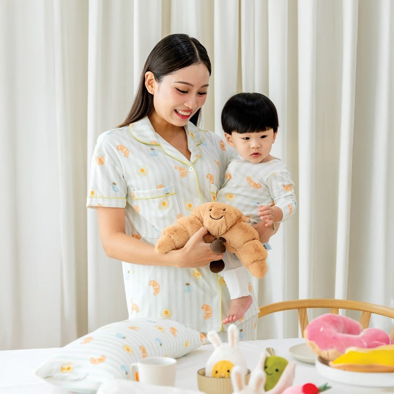 A mother and her baby boy wearing matching sleepwear sets from Le Petit Society, featuring a print of breakfast food and pastel green stripes.