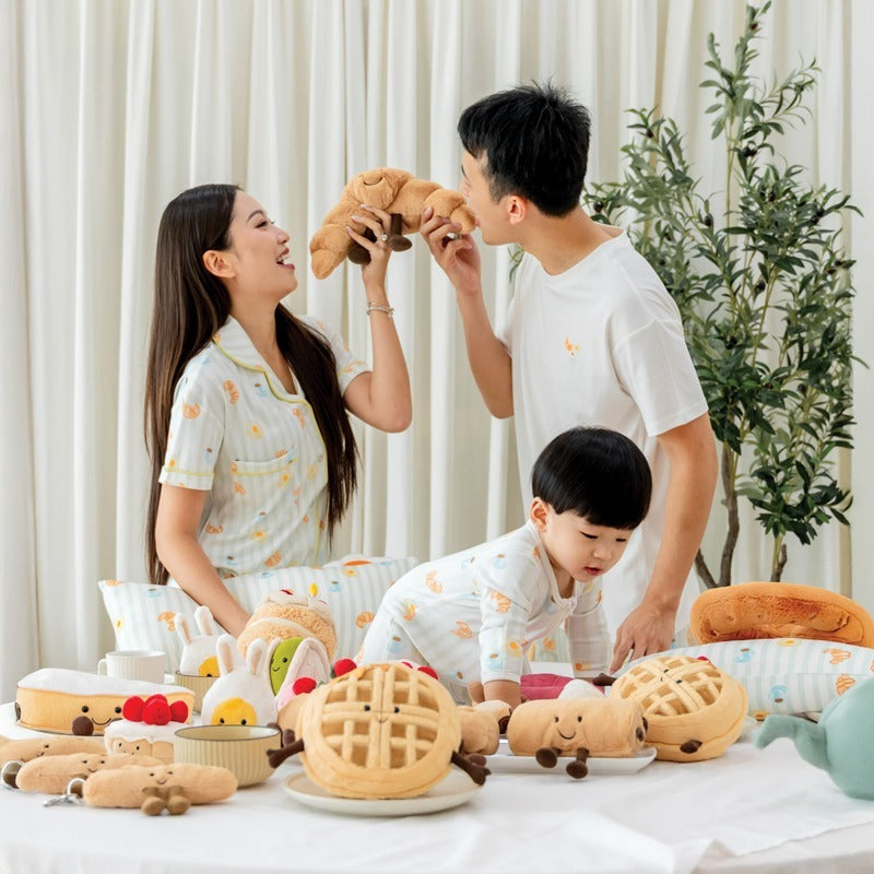 A family of three — mother, father, and baby boy — wearing matching outfits featuring a print of breakfast food from Le Petit Society.