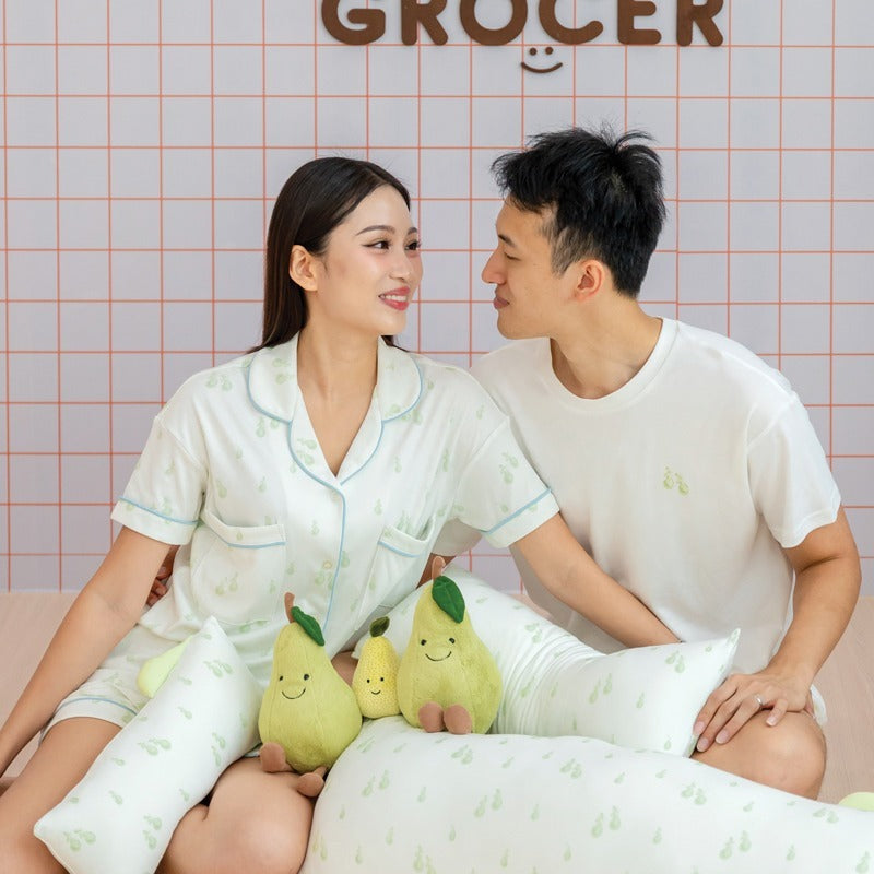 A husband and wife wearing coordinated outfits from Le Petit Society's sleepwear collection, both featuring a matching green pear print.