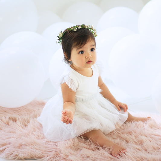 A baby girl dressed as a flower girl in a white bubble dress by Le Petit Society.