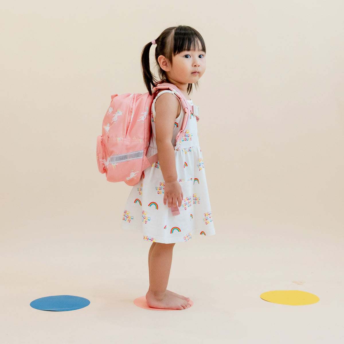A preschool girl carrying a pink unicorn print school bag.