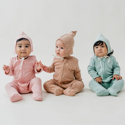 Three babies in matching sets of bonnet hats and zip sleepsuits in pink, brown and mint blue from Le Petit Society.