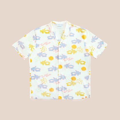 White short-sleeve men’s button-up shirt from Le Petit Society with camp collar in colorful dragon playground print and sun print in pastel blue, yellow, green, and pink.