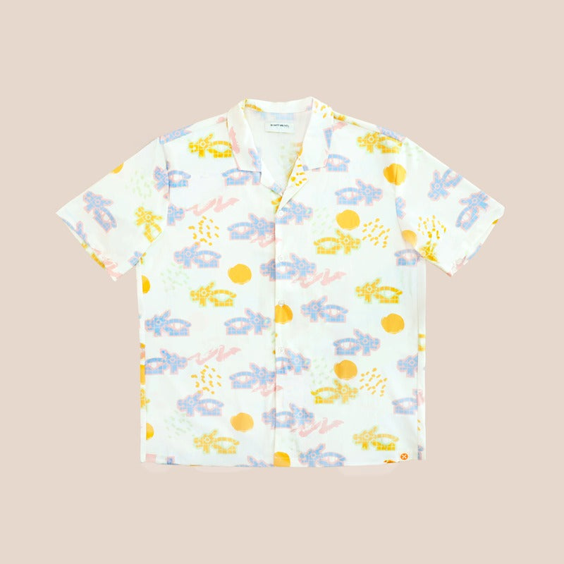 White short-sleeve men’s button-up shirt from Le Petit Society with camp collar in colorful dragon playground print and sun print in pastel blue, yellow, green, and pink.