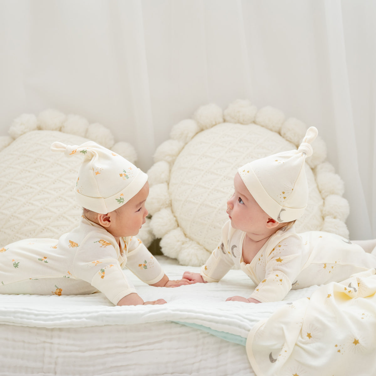 Two babies wearing organic zip sleepsuits and hats with adorable prints from Le Petit Society. 