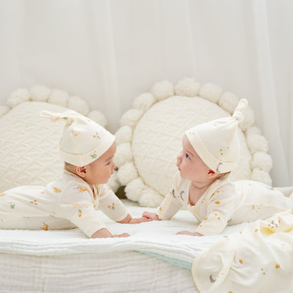 Two babies wearing organic zip sleepsuits and hats with adorable prints from Le Petit Society. 