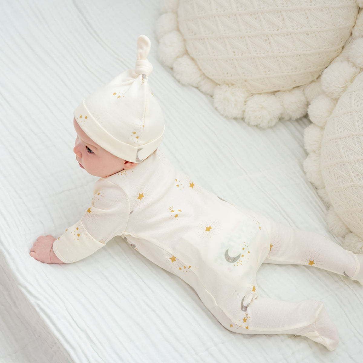 A baby wearing an organic zip sleepsuit with foldable mittens and footies by Le Petit Society, featuring a print of moon and stars over a cream base.