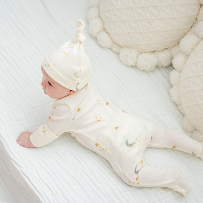 A baby wearing an organic zip sleepsuit with foldable mittens and footies by Le Petit Society, featuring a print of moon and stars over a cream base.