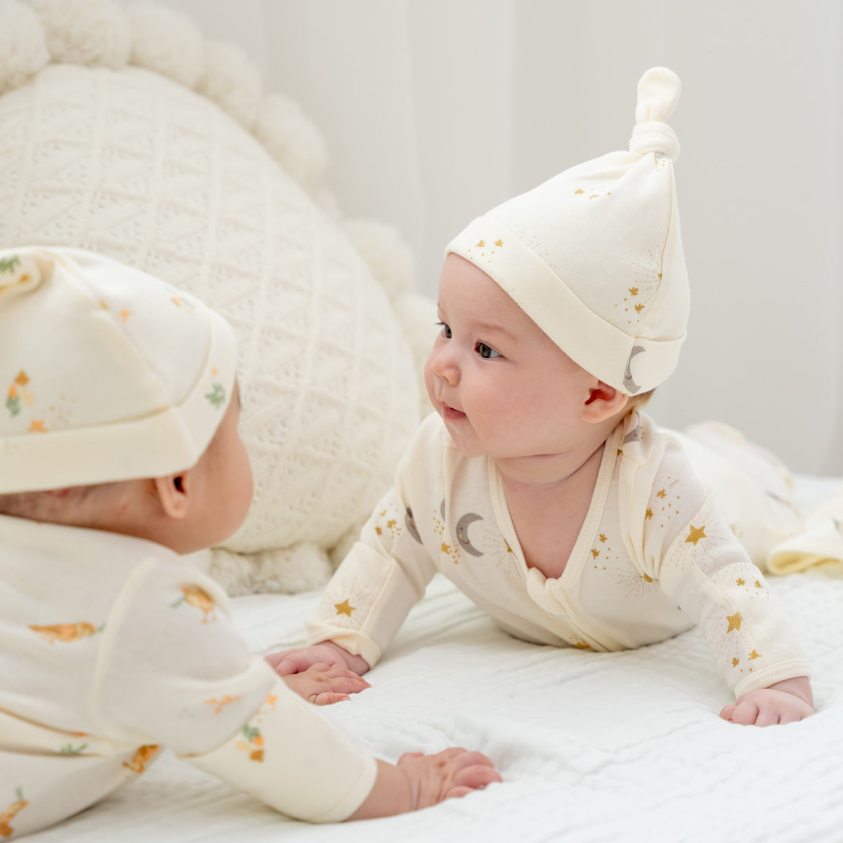 A baby wearing an organic zip sleepsuit with foldable mittens and footies by Le Petit Society, featuring a print of moon and stars over a cream base.
