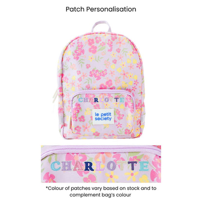 A purple preschool bag with a floral print and personalised name patches.