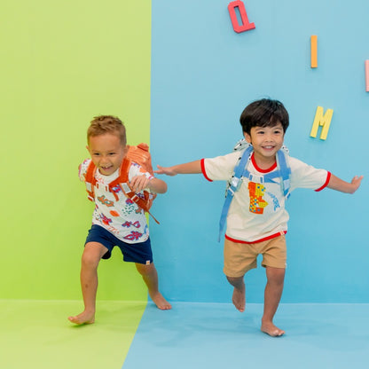 Two preschoolers running forward with school bags on their backs. 