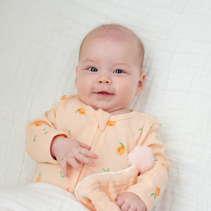 A baby in a coral pink zip sleepsuit with a print of peaches. 