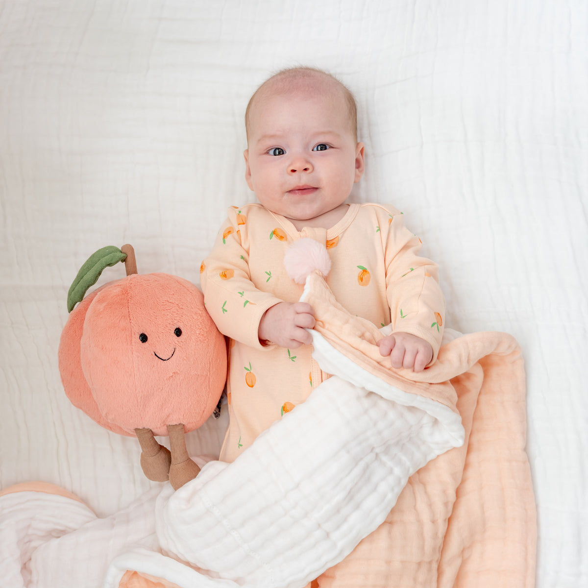 A baby wearing a coral pink zip sleepsuit in peach print with an orange blanket.