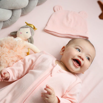 A baby wearing an organic zip sleepsuit in pink by Le Petit Society.