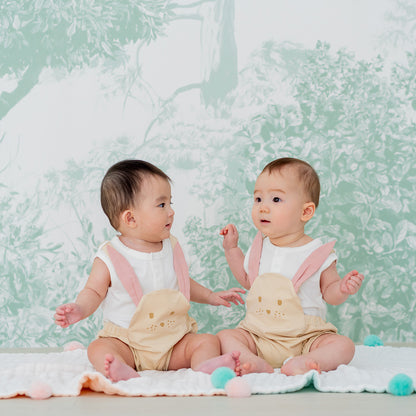 A pair of babies wearing beige animal rompers by Le Petit Society, which come with a rabbit's face in the front.
