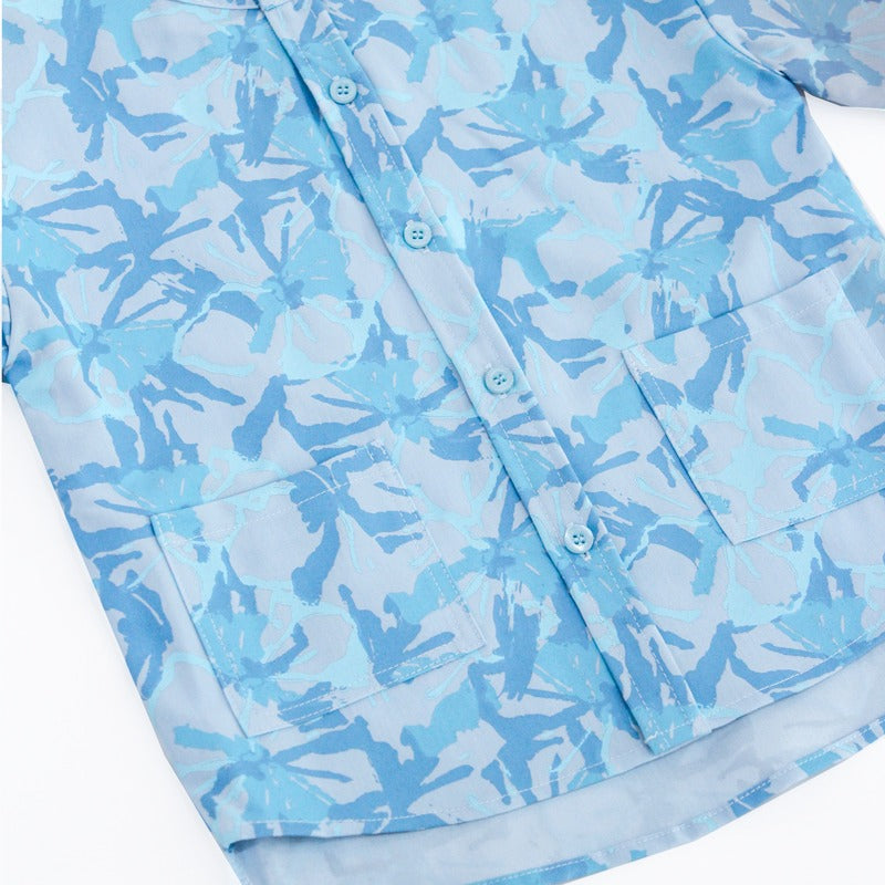 Close-up of the light blue boys’ shirt from the Le Petit Society x Sheila Sim CNY 2026 collection, showing the tonal floral horse print, front buttons, and two patch pockets. The fabric pattern features layered shades of blue on a soft blue base.