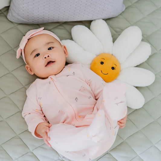 A baby wearing a pink zip sleepsuit and bow headband in a rabbit print by Le Petit Society,