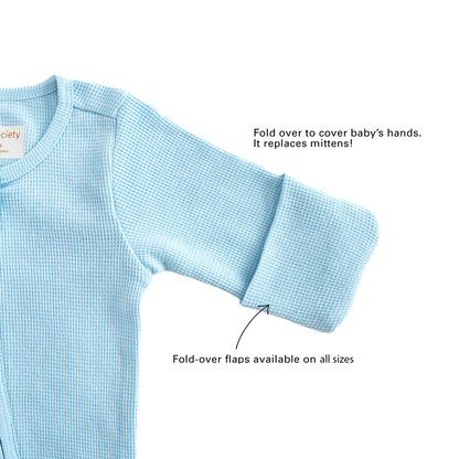 A baby organic zip sleepsuit in blue by Le Petit Society, with fold over flaps at the sleeves to cover a baby's hands, acting as a substitute for mittens.