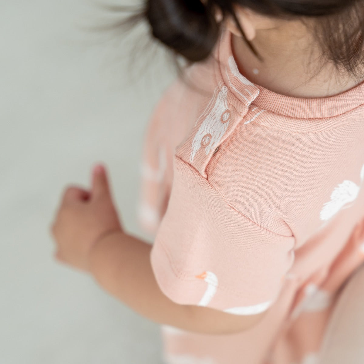 A girl toddler wearing a peach-coloured organic dress adorned with a print of swans from Le Petit Society.