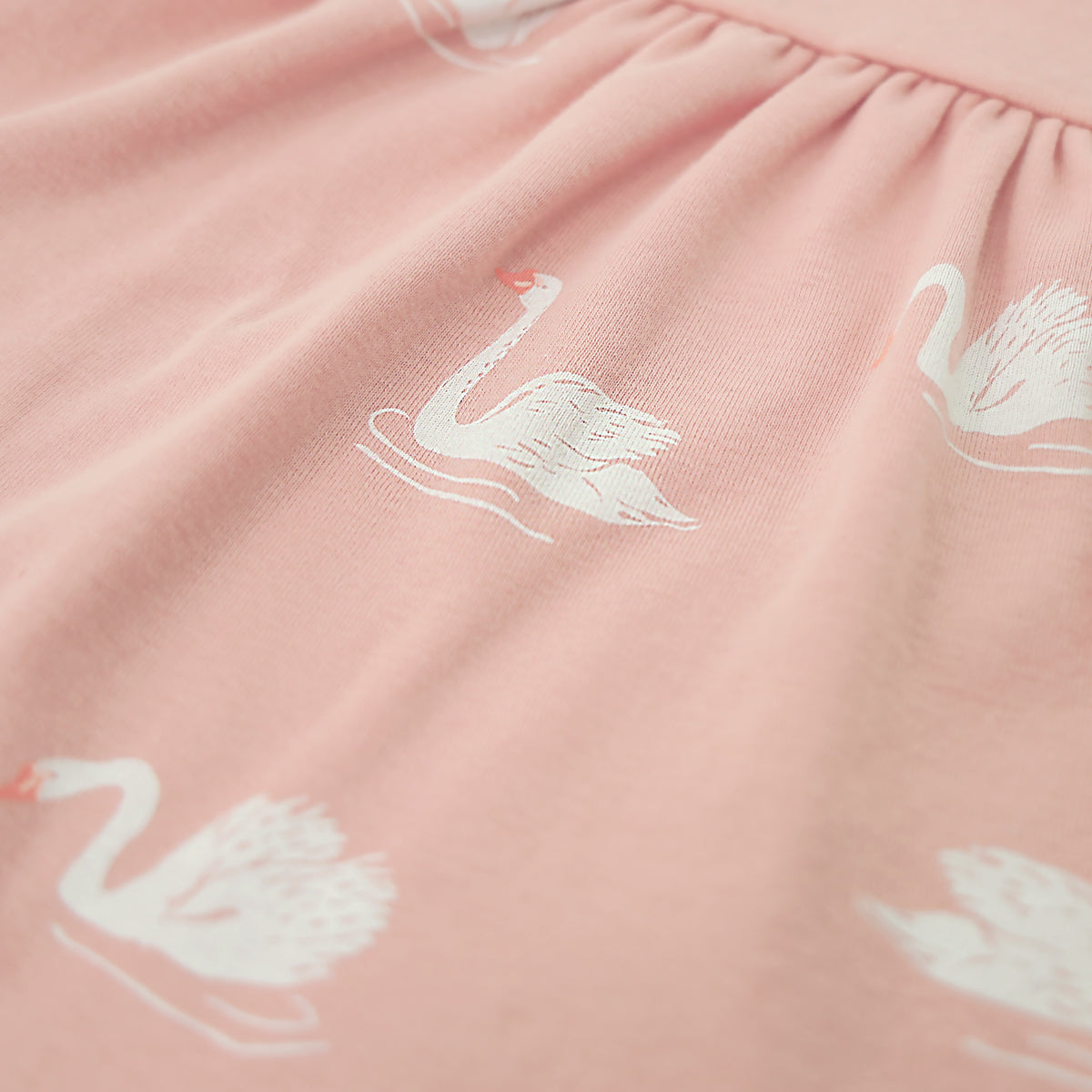 A close-up of the print of a peach-coloured, girl's organic dress from Le Petit Society, featuring a print of swans.
