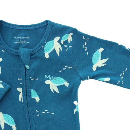 A close-up of a personalised name embroidery on an organic zip sleepsuit in turtle print by Le Petit Society.