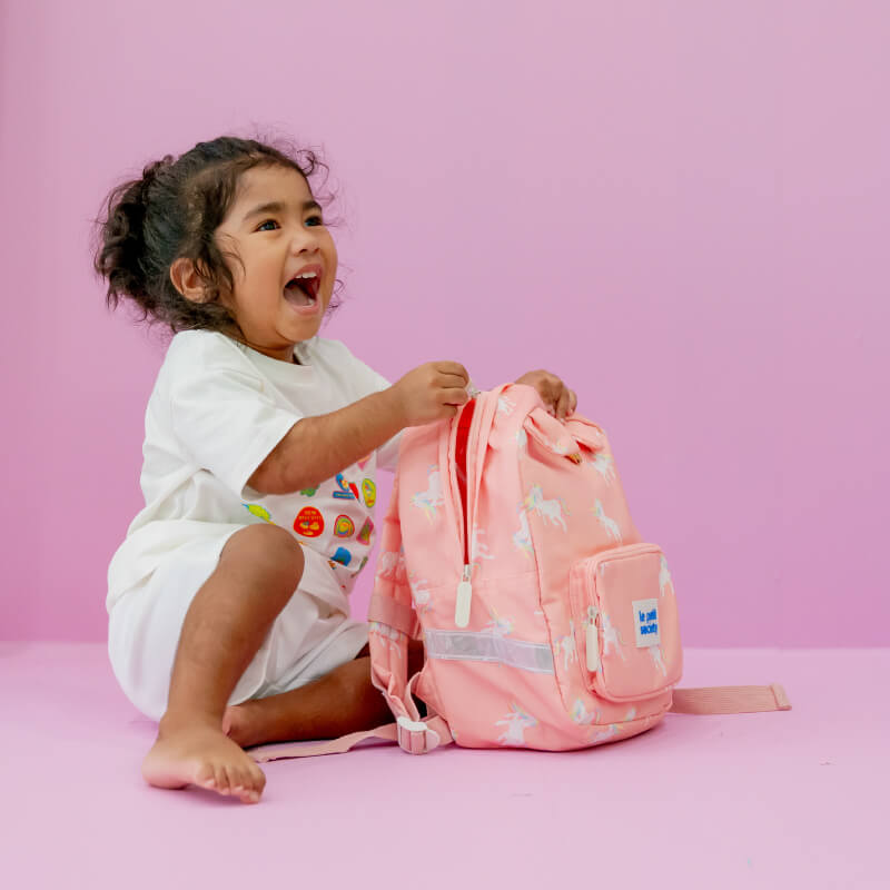 Toddler smiling with a pink unicorn print preschool bag.