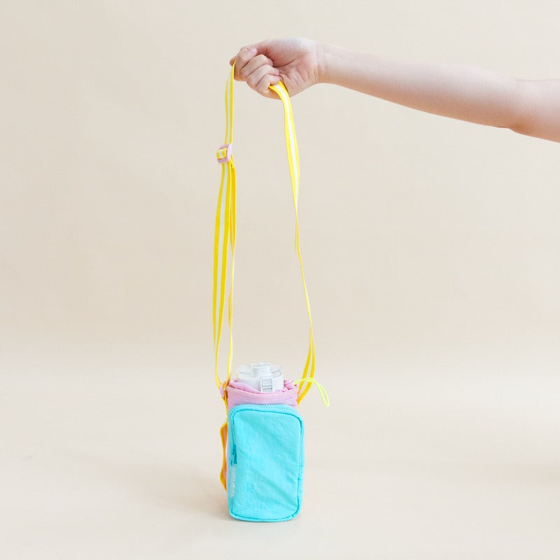 A hand holding on to the adjustable strap of a water bottle sling bag.