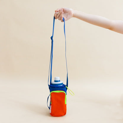 A hand holding on to the adjustable strap of a water bottle sling bag 