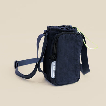 A dark blue water bottle sling bag with an adjustable strap and a front pocket 