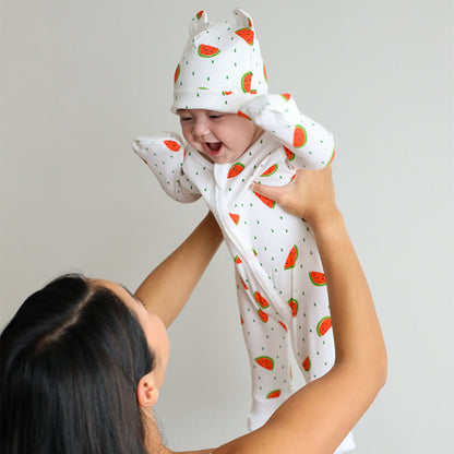 A baby wearing Le Petit Society's organic zip sleepsuit and bear hat in watermelon print.
