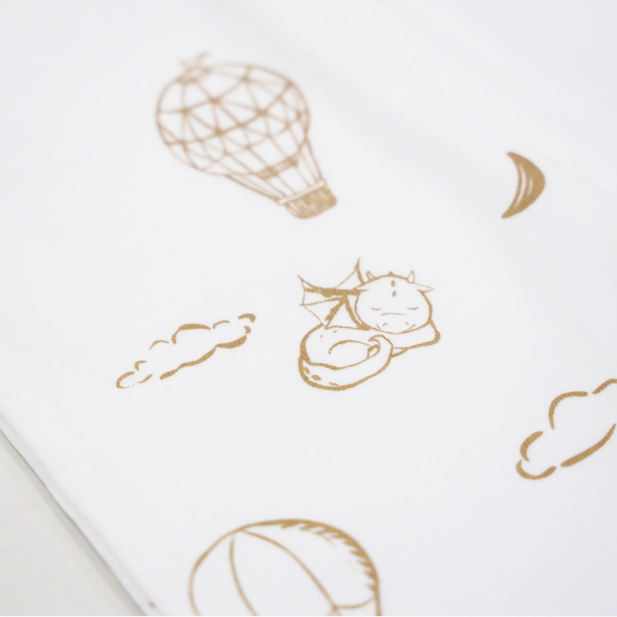 A close-up of the print of Le Petit Society's baby organic zip sleepsuit in dreamy dragon print, which consists of  sleeping dragons, crescent moons, clouds and hot air balloons.